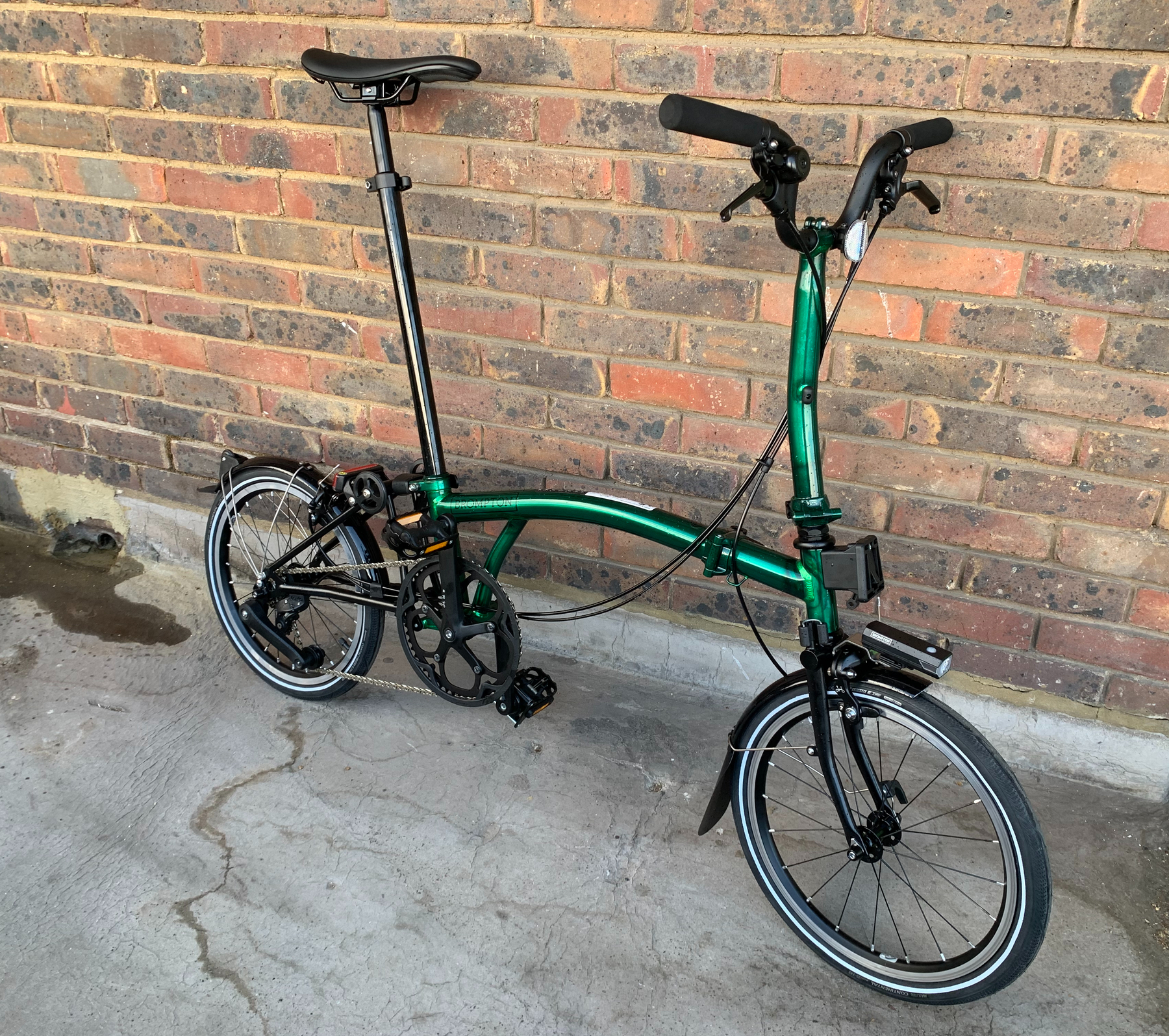 Emerald green Brompton P-Line folding bike leaning against a brick wall