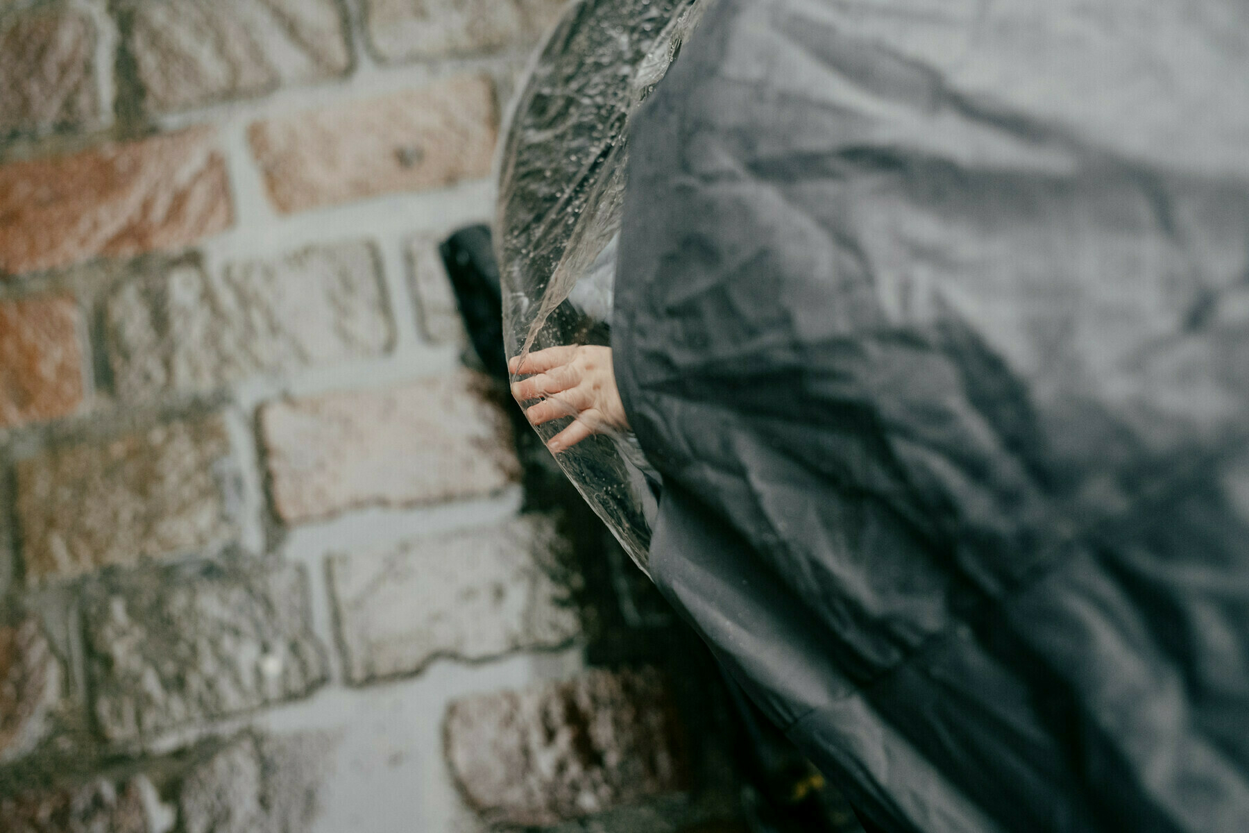 looking down at a baby's hand pushing out against a pram's clear plastic raincover, with out of focus cobblestones in the background