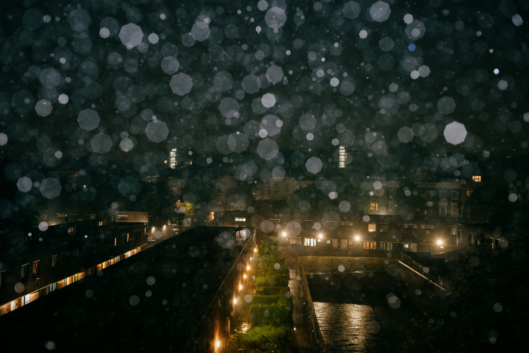 Night view of a housing estate in London seen from a high vantage point. It's raining heavily and the raindrops are lit up with flash, forming shimmering octagons across the frame