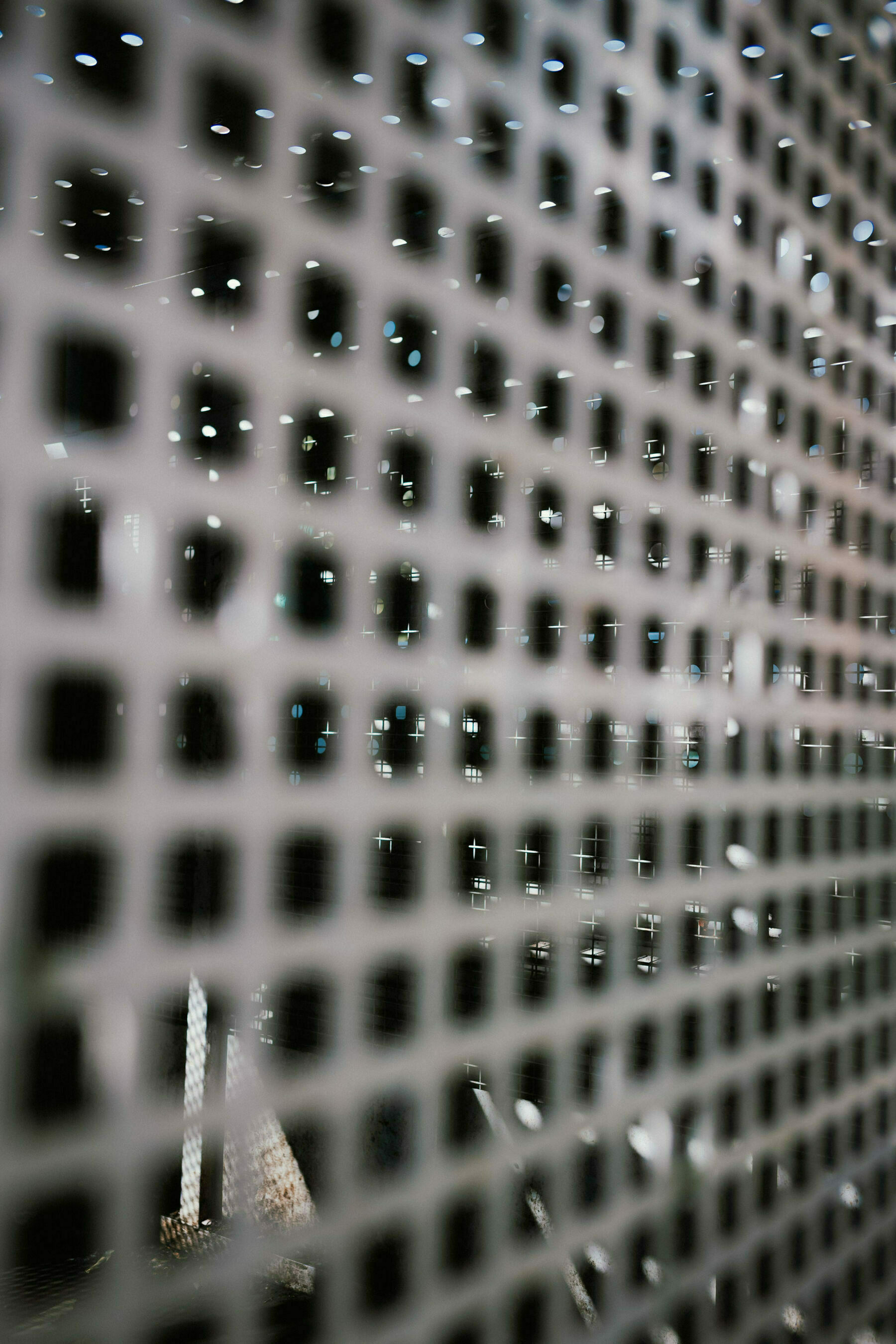 Out of focus grille in foreground, circles of sunlight picking out intersections on metal grille seen through the foreground one. 