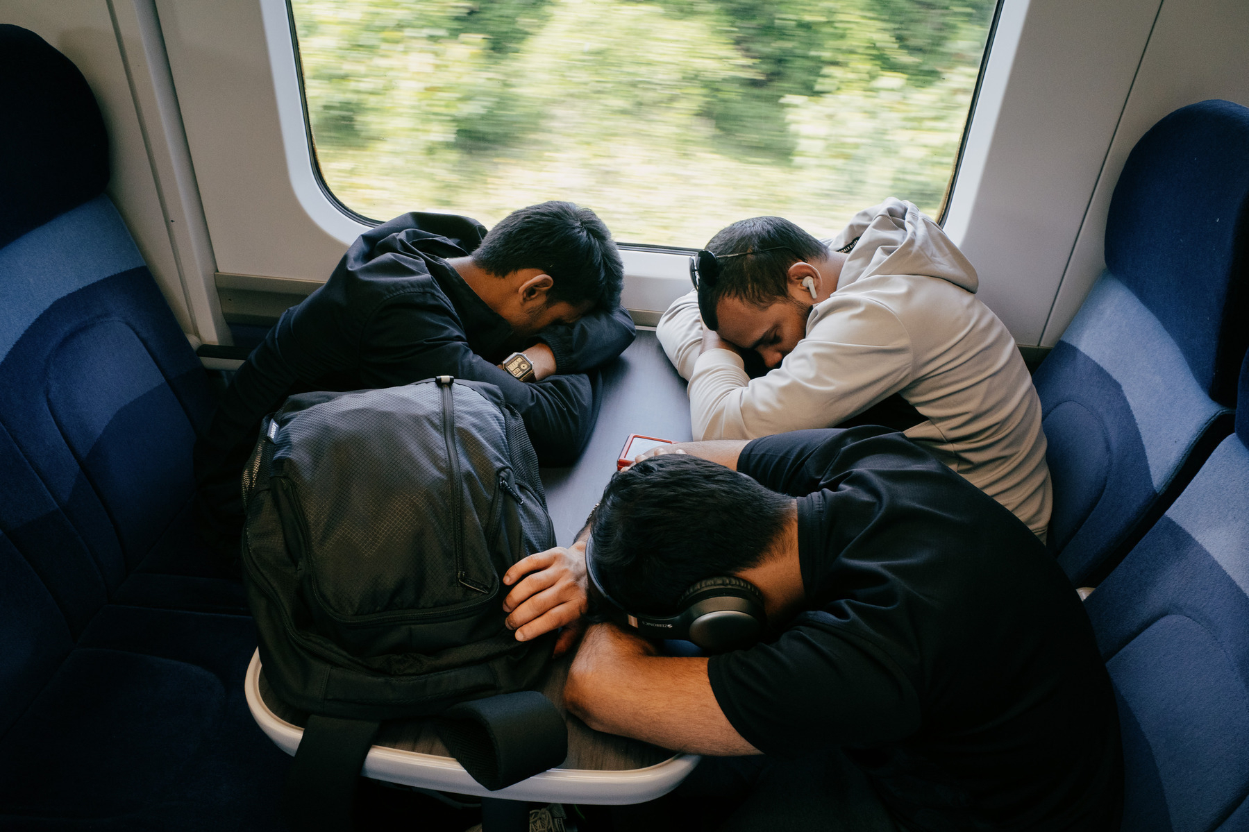 Three men sleeping with their heads on the table of a train